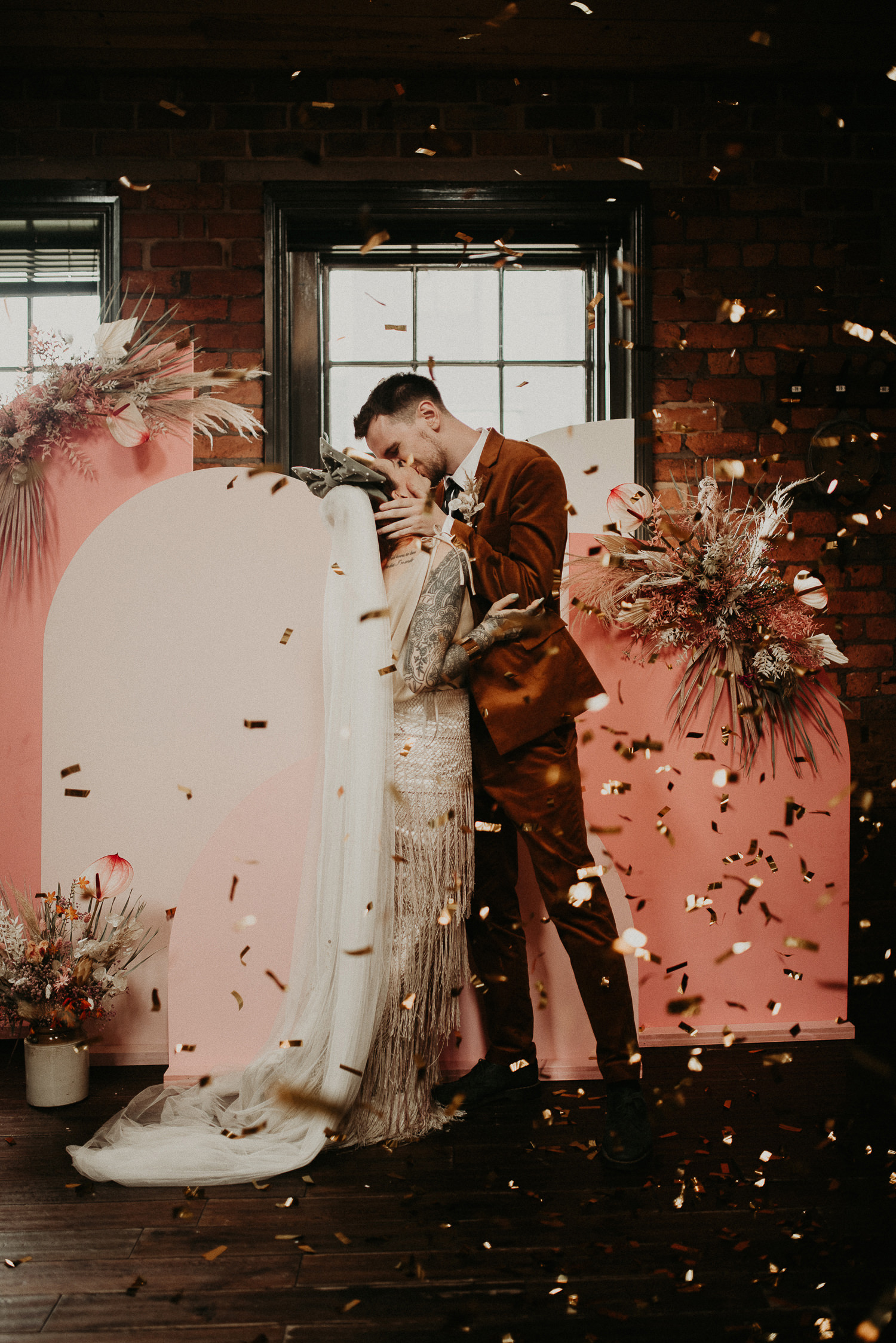 A confetti shot at The Chimney House in Kelham Island in Sheffield. An alternative couple kiss under a shower of gold confetti.