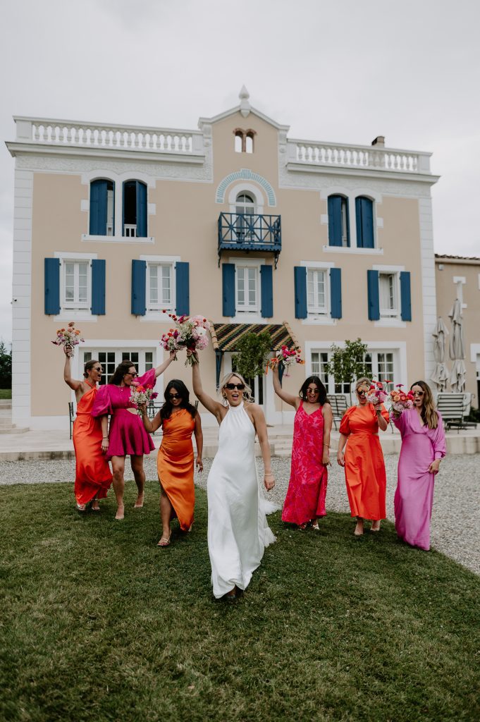 A bride and her bridesmaids walking away from the villa at Chateau Canet with their bouquets in the air. The bridesmaids are wearing pink dresses and all the bouquets are pink.