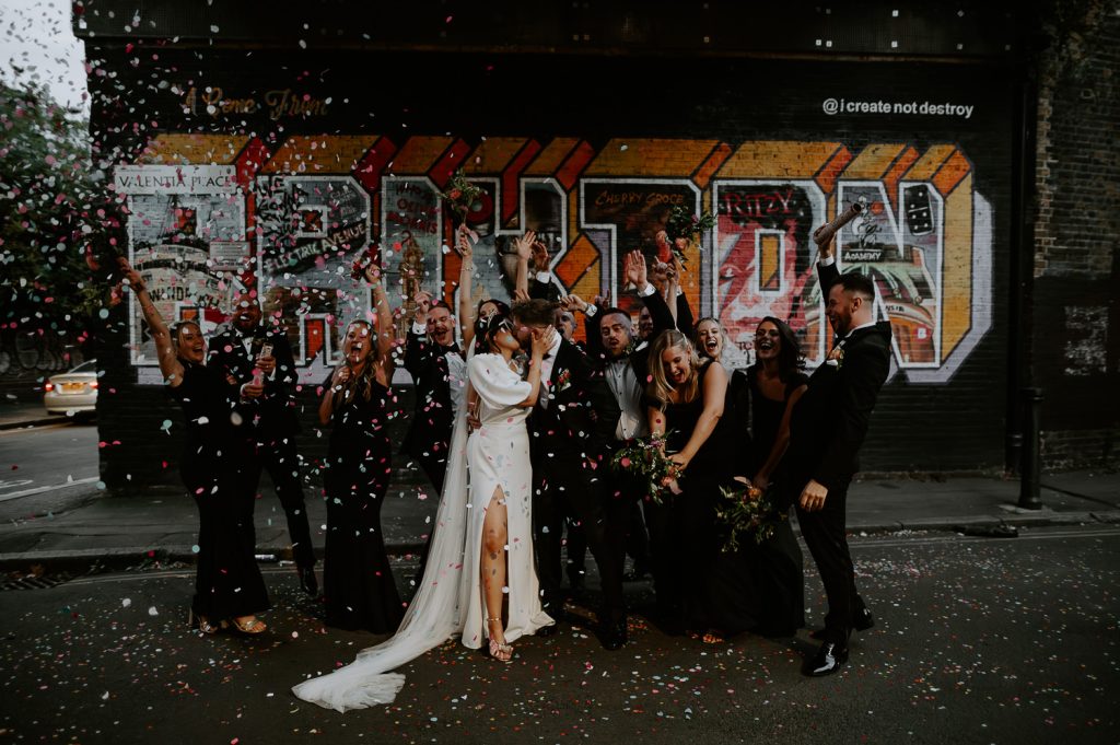 A bride, Groom and their wedding party set off confetti canons outside the Brixon Mural.