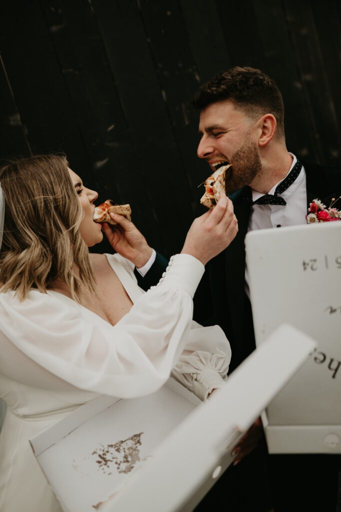 Bride and Groom feed each other pizza at their alternative wedding at The Giraffe Shed.