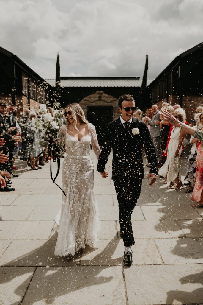 A bride and groom walk through a tunnel of their guests throwing confetti.