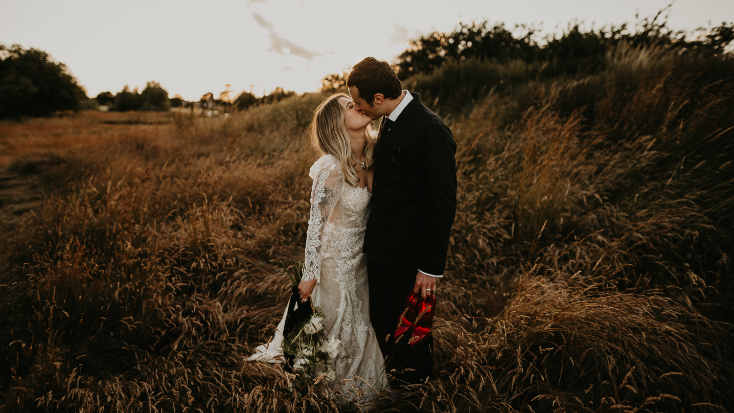 A bride and groom kiss in the long grass at their wedding at Willow Marsh Farm.