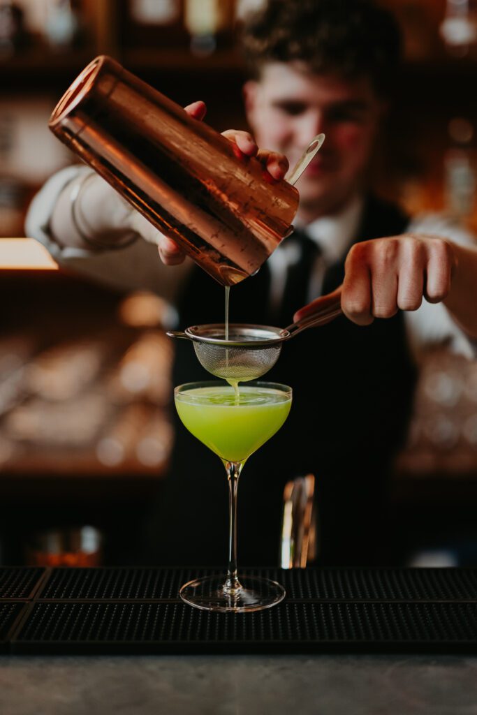 Barman pours green cocktail at 100 Barrington.