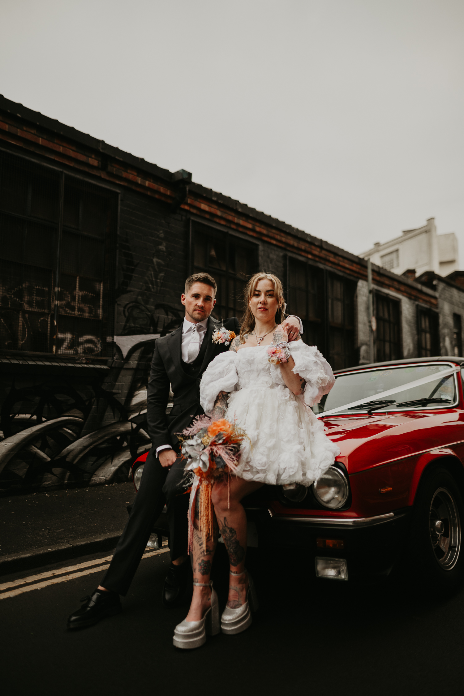 Bride and groom sit on a vintage car at one of the best Birmingham Wedding Locations.
