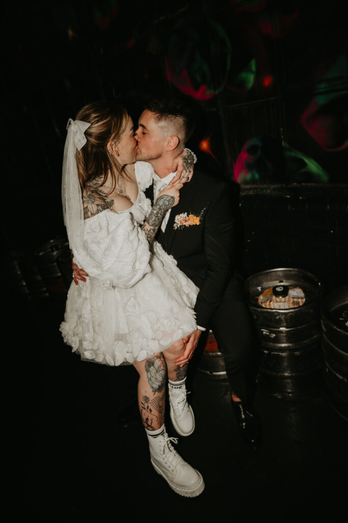 Bride and Groom kiss whilst sat on a beer keg at NQ64 in Birmingham, one of the best Birmingham Wedding Locations for alternative couples.