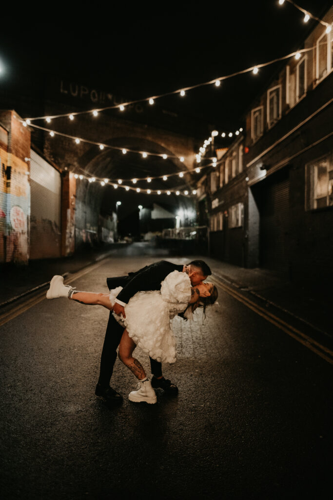 A bride and groom dip kiss under the string lights in Digbeth on their wedding night.