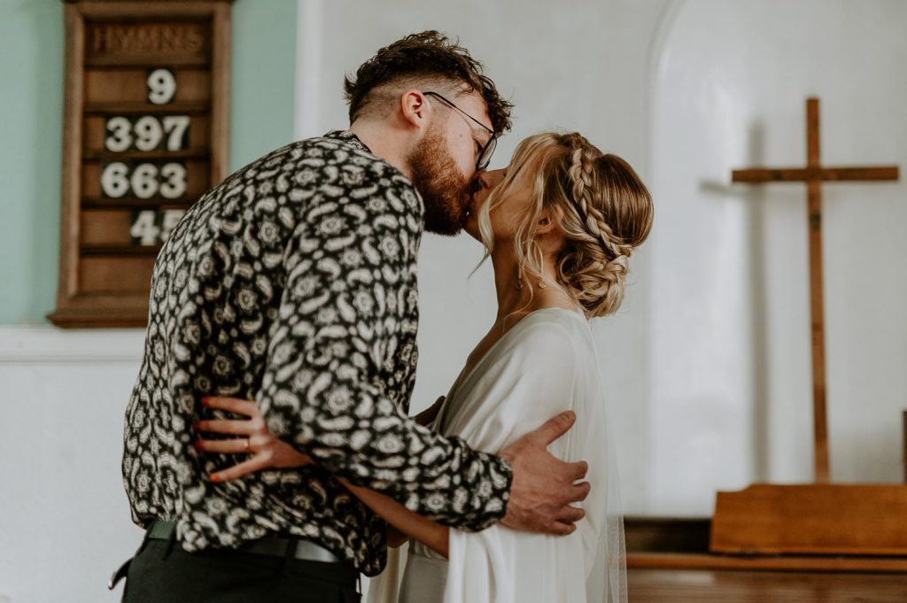 A bride and groom kiss at their wedding in a small church in Bristol.