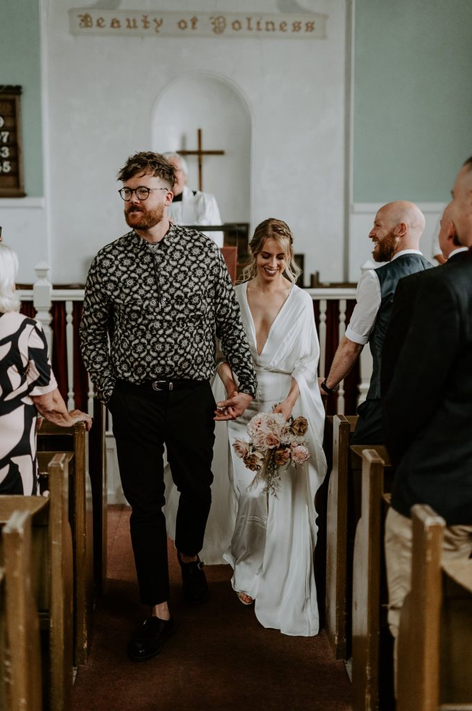 A bride and groom walk back up the aisle in a small church in Bristol.