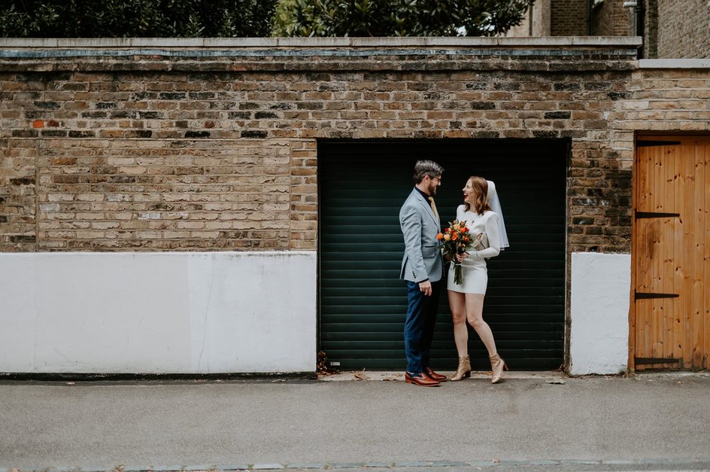 Whilst waiting for a taxi to Chelsea Town Hall and bride and groom laugh in the doorway of a black garage.
