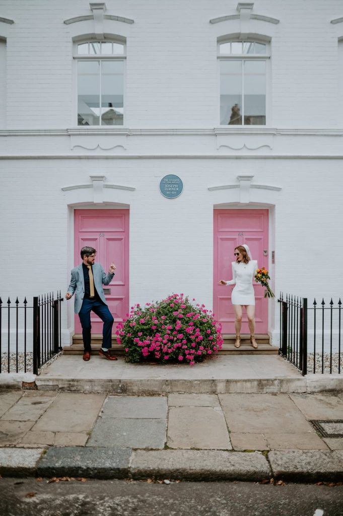 London wedding at Chelsea Town Hall. A couple have portraits outside a couple of pink doors in Chelsea. The bride is wearing a short Neta Porter Dress and vintage headpiece.