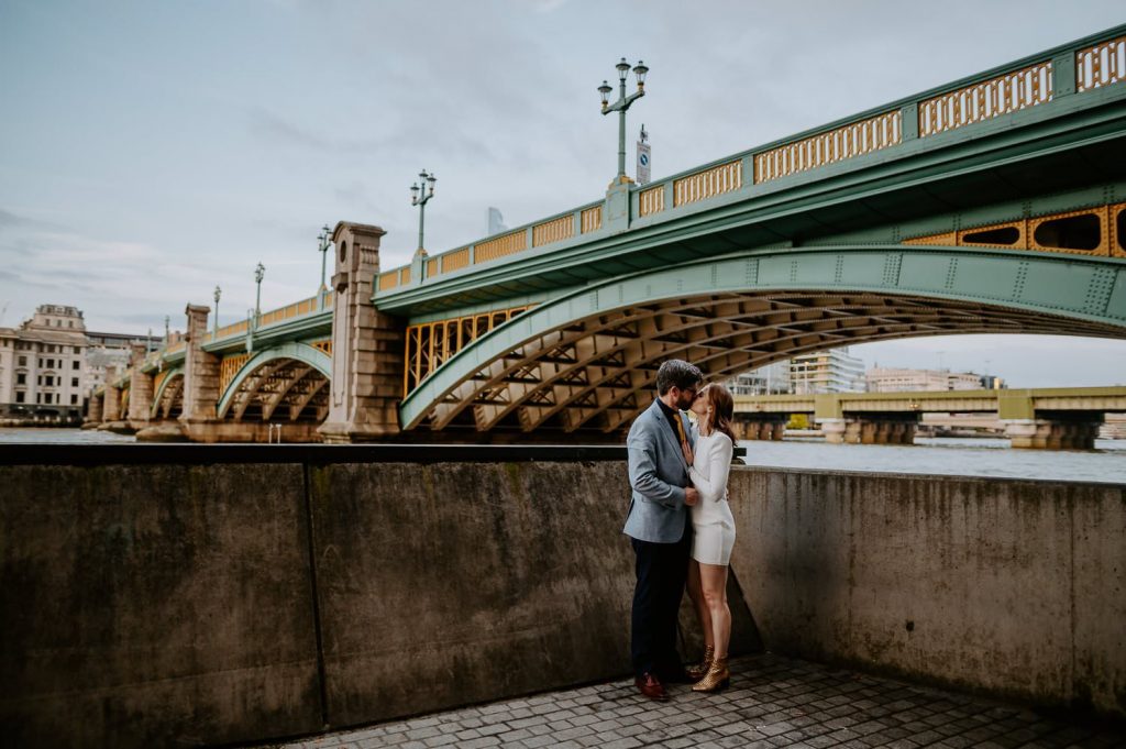A bride and groom kiss under the Southwark Bridge in London.