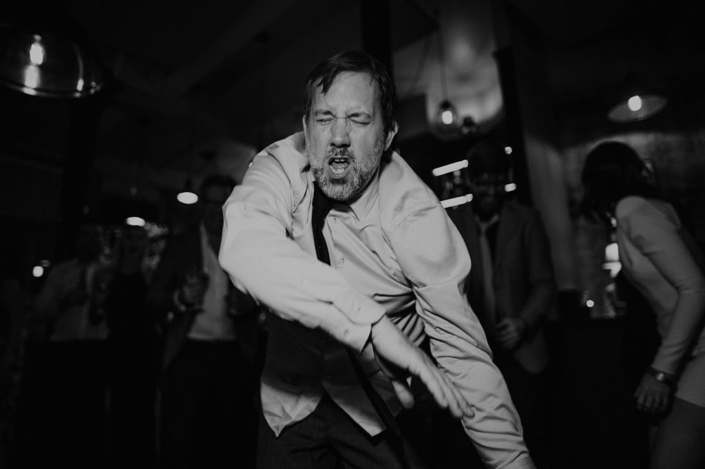 A black and white shot of a wedding guest dancing.