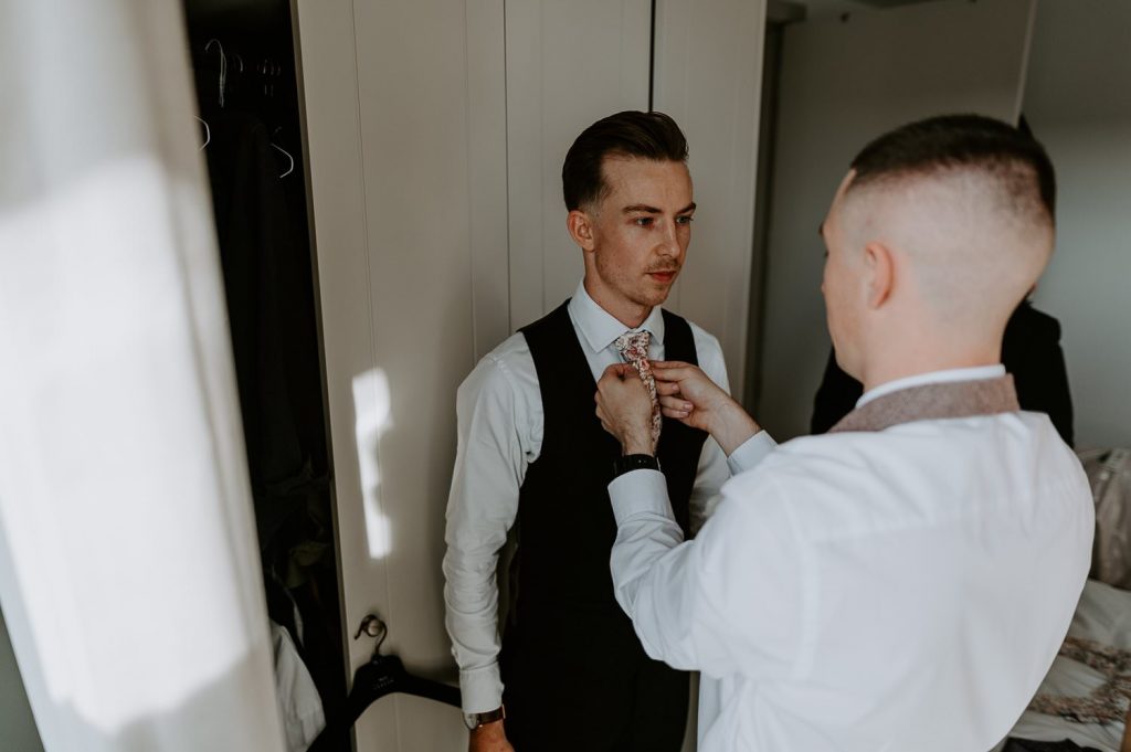 A groomsmen fixes a grooms tie on his wedding morning.