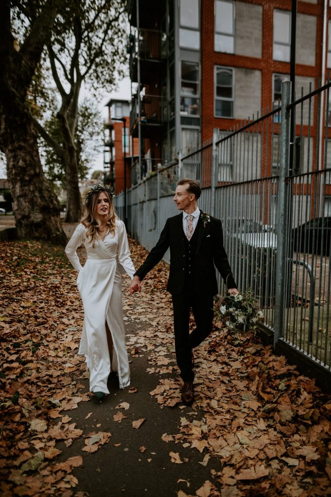 A bride and groom walk through the leaves in a park in Clapton in Autumn.