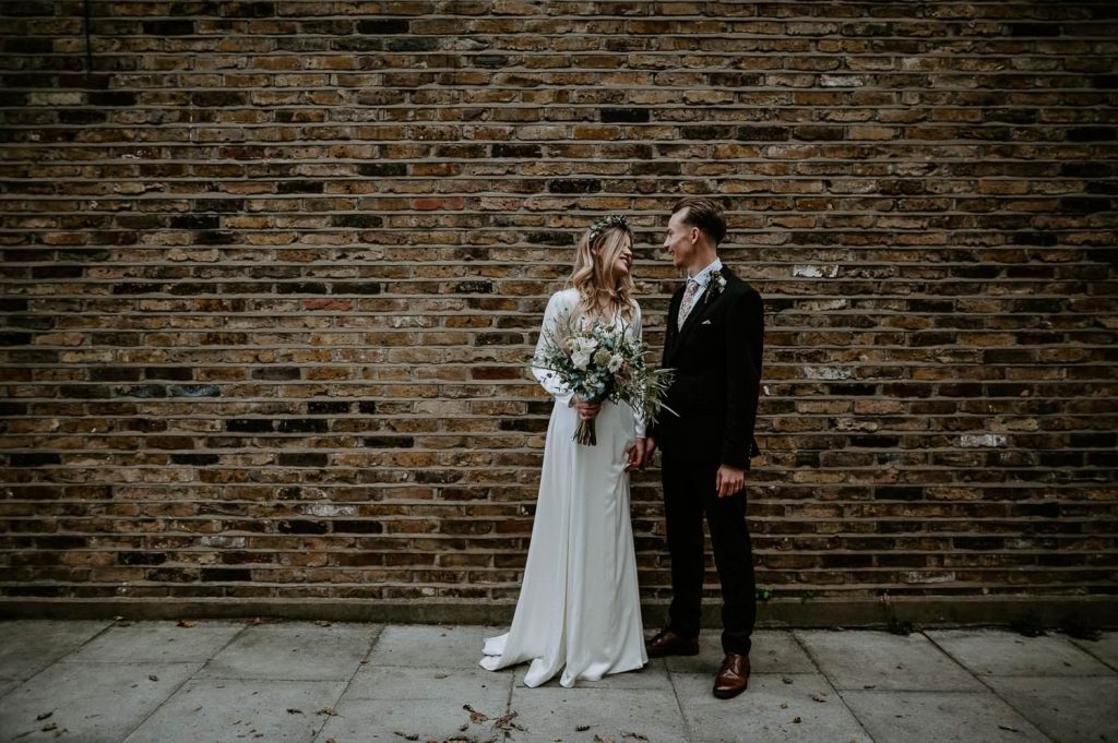 A minimal landscape shot of a bride and groom in front of a brick wall.