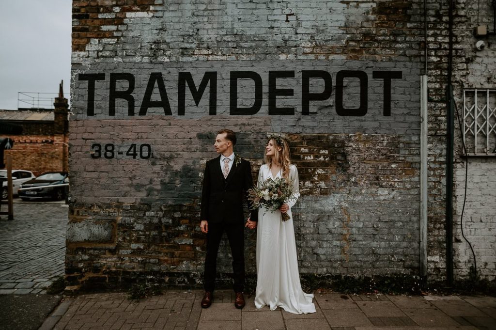 A bride and groom outside the Tram Depot typeface wall at Clapton Country Club.