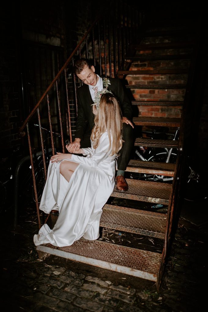 An evening flash shot of a bride and groom sat on some steps at Clapton Country Club in London.