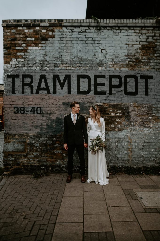 A bride and groom stand next to the TRAM DEPOT typeface at Clapton Country Club.