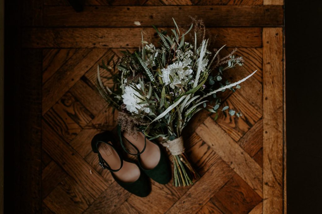 A wedding bouquet with green shoes on the hardwood floor.