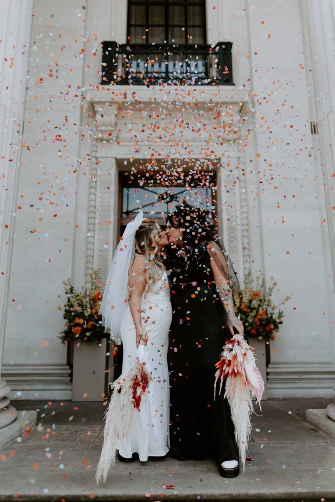 Brides kiss and guests throw confetti at the top of the stairs at Marylebone Town Hall