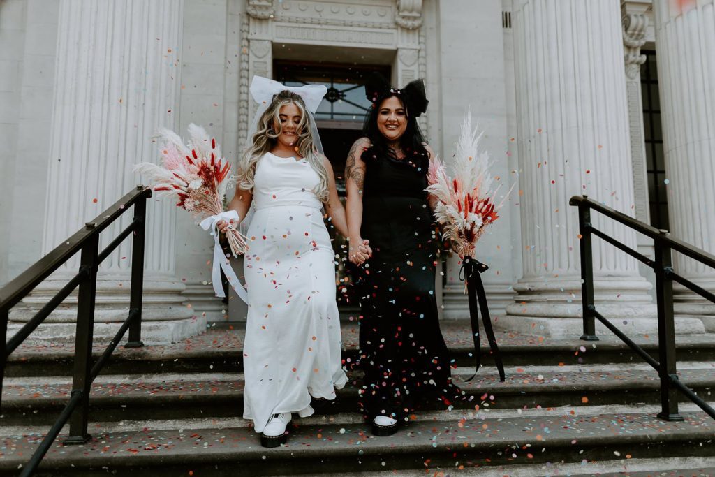 Two brides walk down the outside steps at Marylebone Town Hall in London