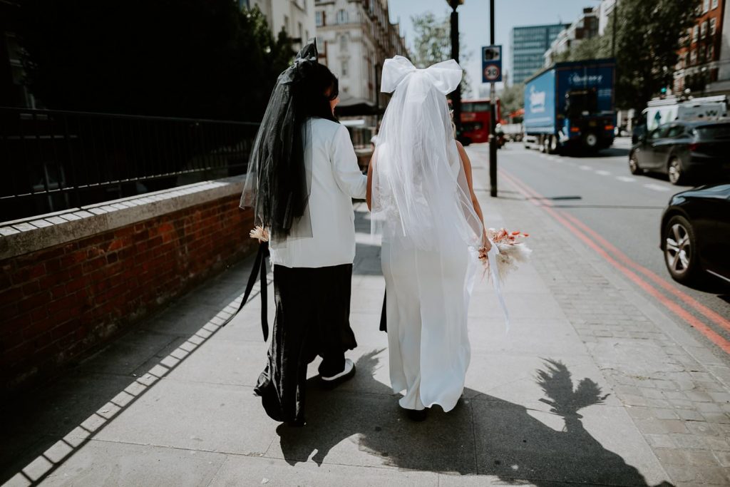 A behind shot of two brides walking to their ceremony at Old Marylebone Town Hall in London.
