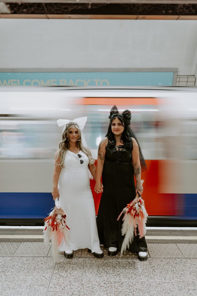 Long exposure of two brides standing in a London tube station as a train passes by.