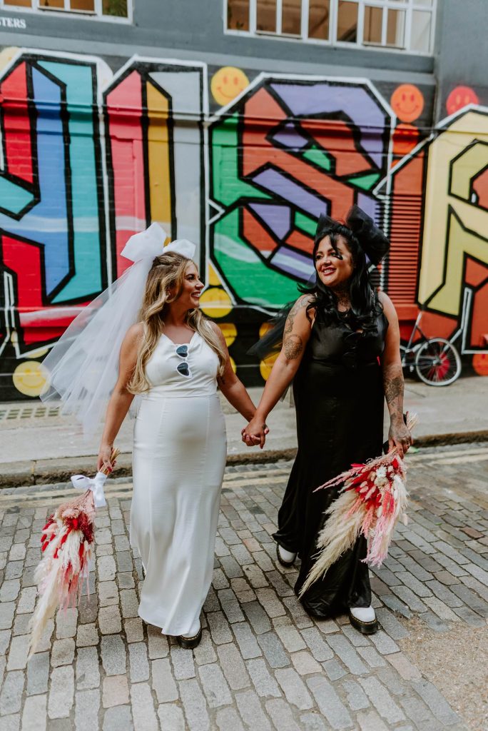 Two same sex brides walk along the street of graffiti in Shoreditch.