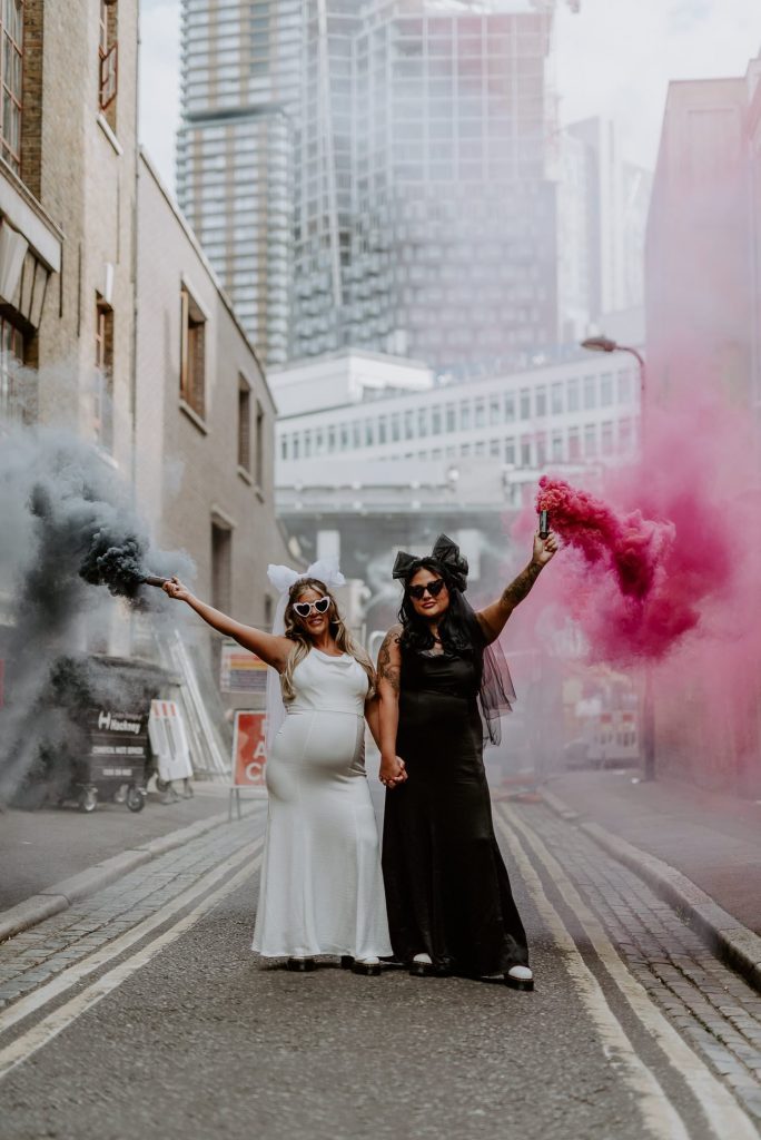 Two same sex brides hold pink and black smoke grenades outside Shoreditch Studios in London.