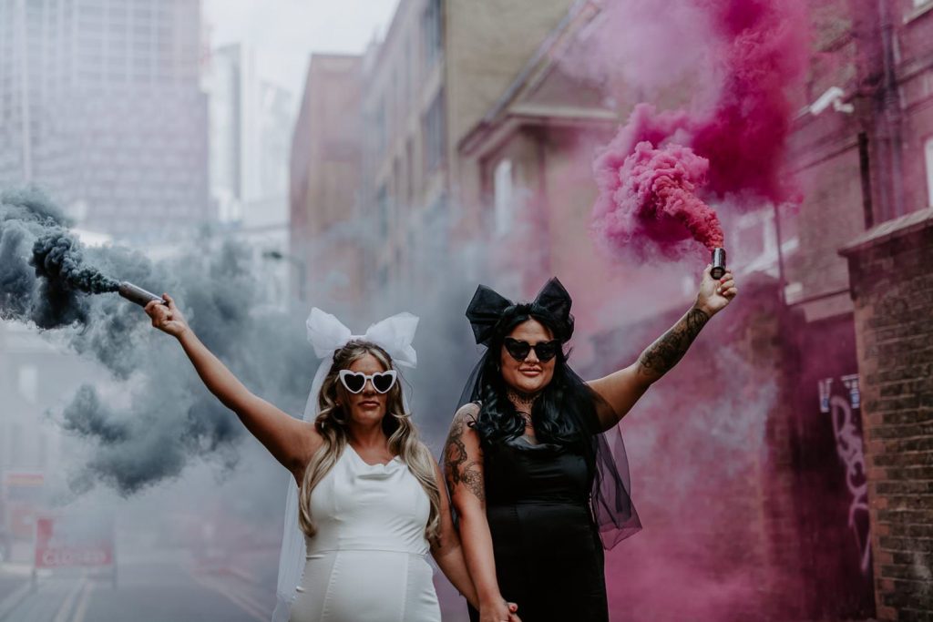 Two same sex brides hold pink and black smoke grenades outside Shoreditch Studios in London.