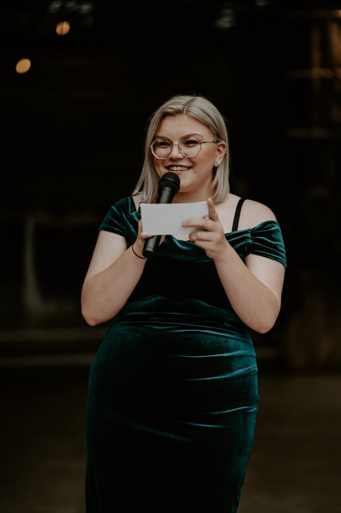 A bridesmaid wearing a green velvet dress gives a speech.