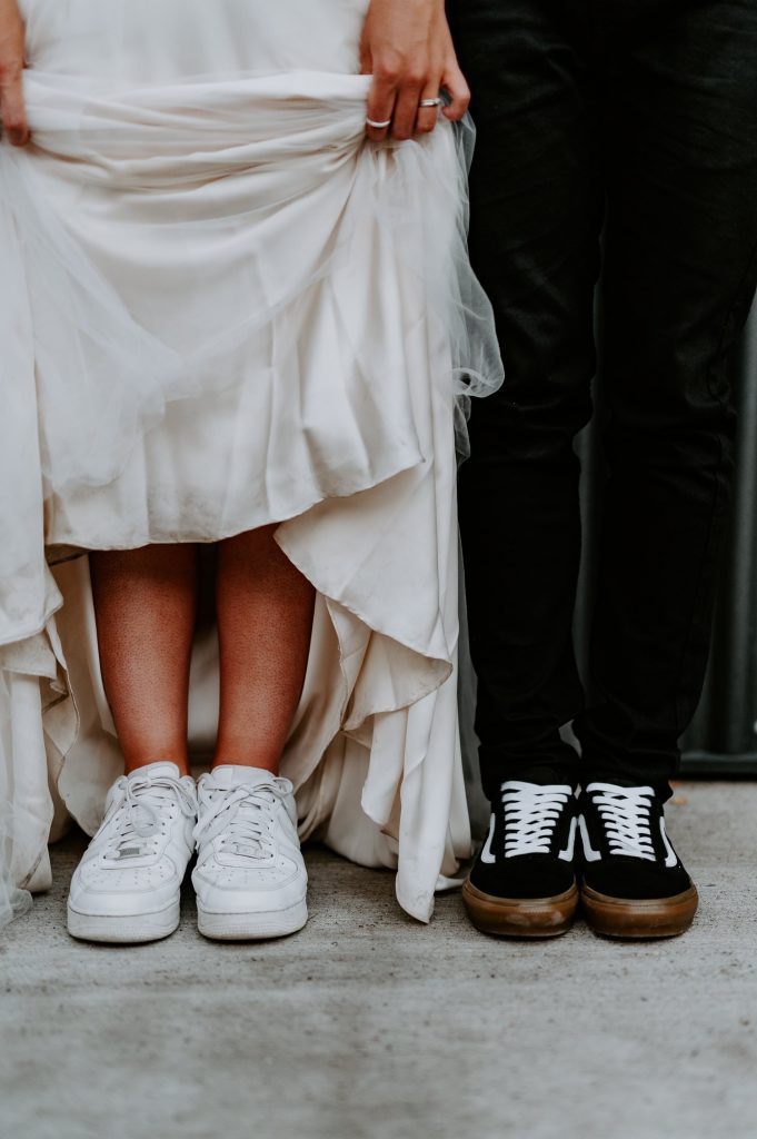 A bride and groom lift their dress and trousers to show that they are wearing trainers on their wedding day.