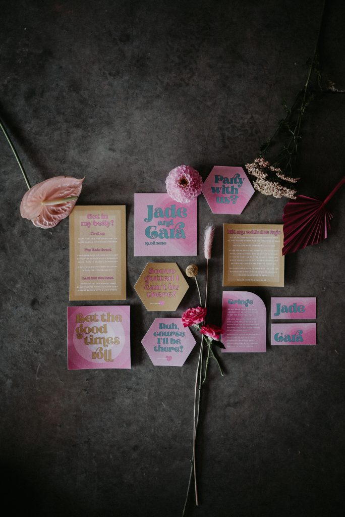 Custom wedding stationery lays on the floor at the giraffe shed. Styled with flowers the pink and yellow stationery pops on the concrete floor.