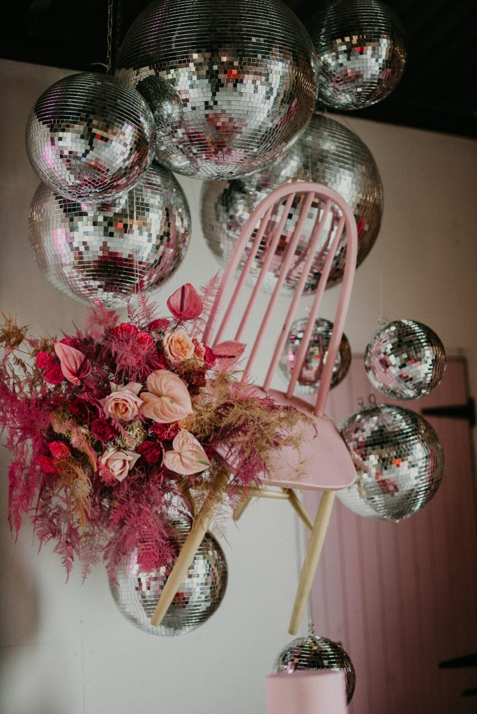 A pink chair hangs from the ceiling surrounded by pink flowers and disco balls. Luna and the Lane's styling at The Giraffe Shed.