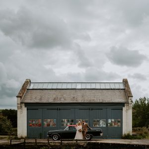 A straight on shot of a bride and groom outside the garages at The Depot in Northampton with the grooms El Camino.