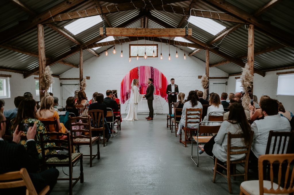 A bride and groom getting married in front of a pink streamer backdrop at White Syke Fields.