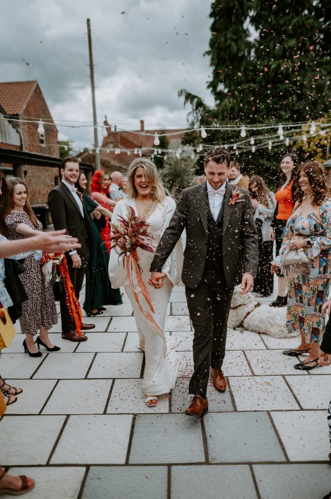 A bride and groom walk through a tunnel of confetti at White Syke Fields.