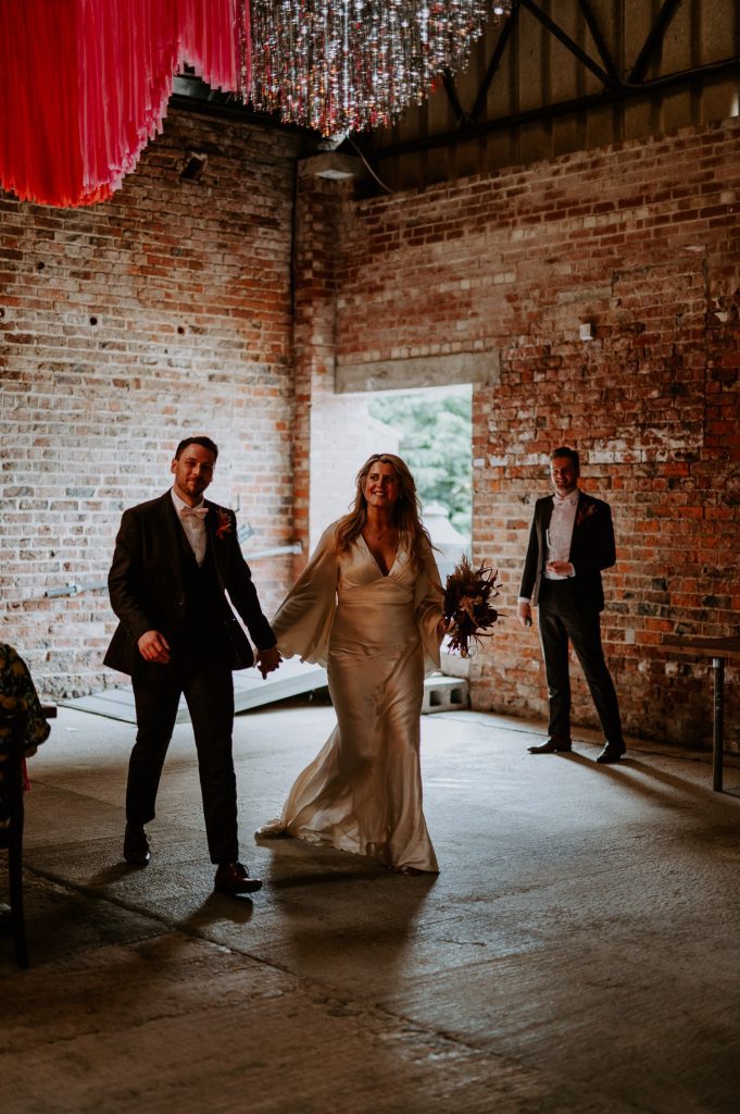 A bride and groom enter the barn to their guests clapping at White Syke Fields.