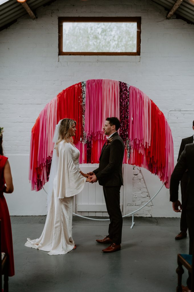 A bride and groom exchange vows in front of their DIY streamer backdrop at White Syke Fields.