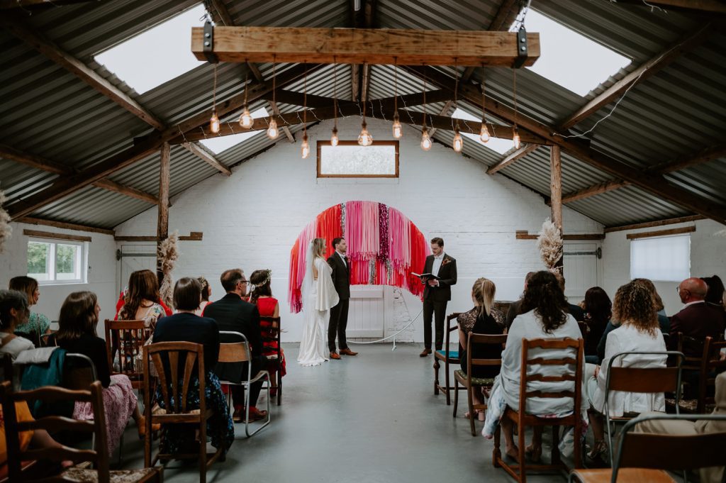 A wide shot of a bride and groom listening to heir celebrant at their wedding at White Syke Fields.