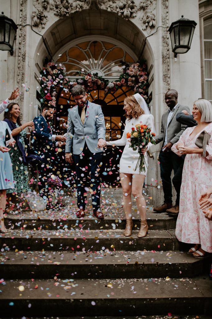 Bride and groom walk down the steps to a shower of confetti at Chelsea Town Hall.