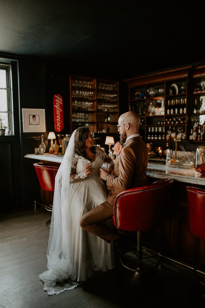 A bride and groom sit having a cocktail at the bar during their wedding at Five Four Studios.