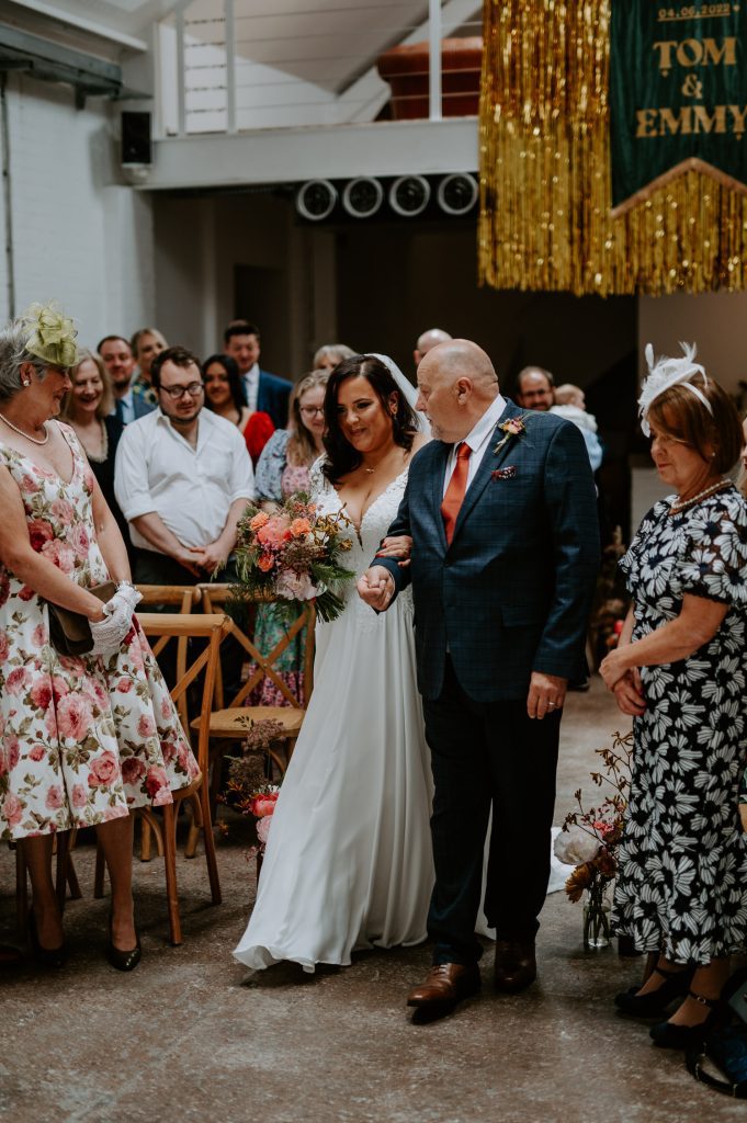 A tattooed bride walks down the aisle with her dad at Five Four Studios.