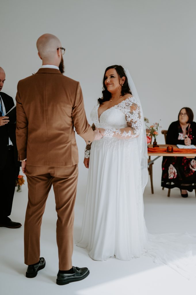 A groom wearing a tobacco suits holds his brides hand a their stylishly colourful wedding at Five Four Studios.