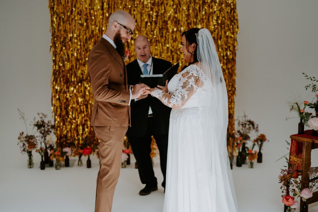 A groom places a ring on his brides hand at Five Four Studios.