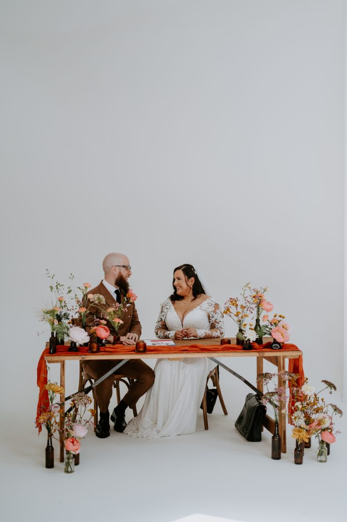 A bride and groom sign the register at their stylishly colour wedding at Five Four Studios whilst being surrounded by vases of flowers.