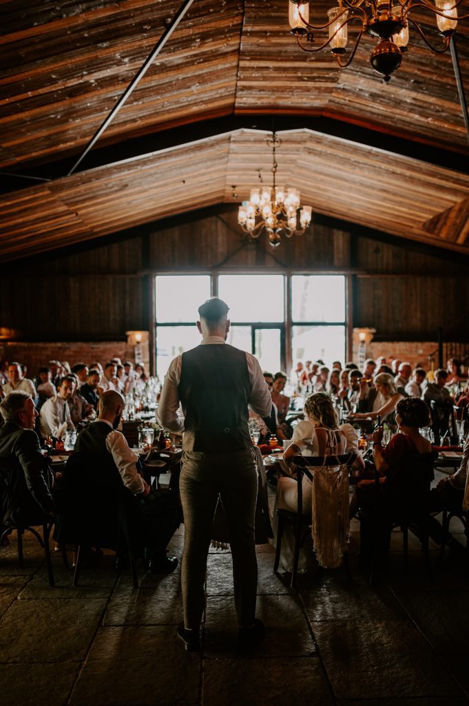 A wide shot from behind of a groom delivering his speech at The Willow Marsh.