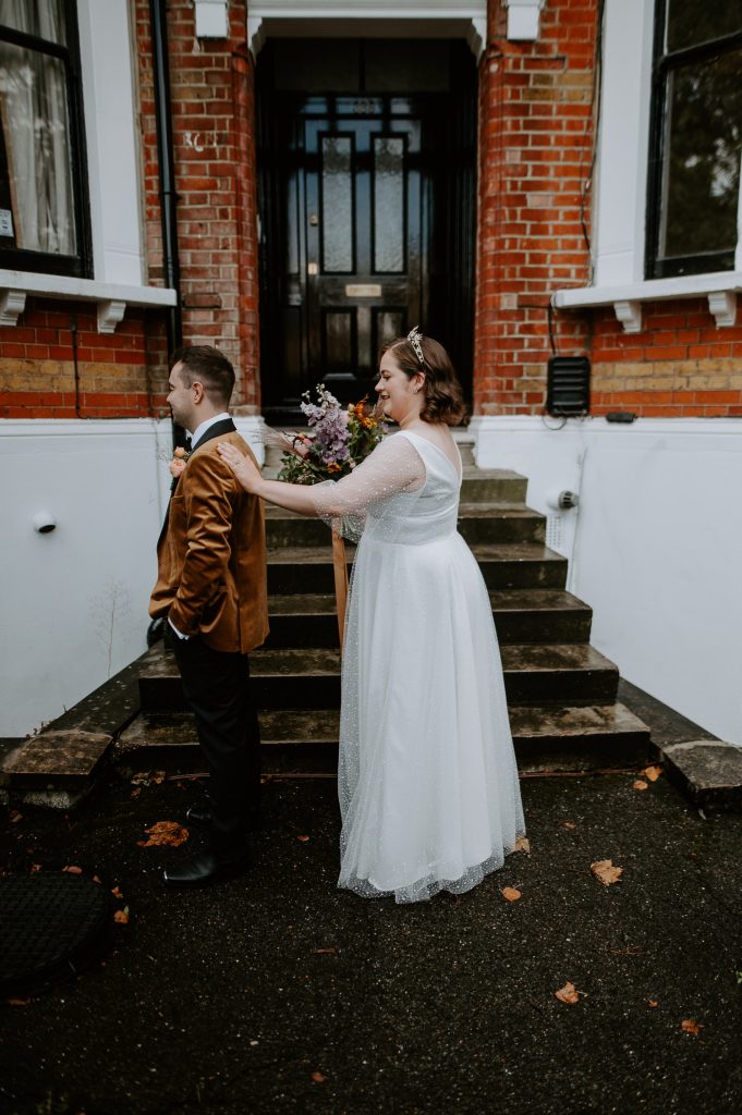 Bride taps groom on the shoulder for first look in London.