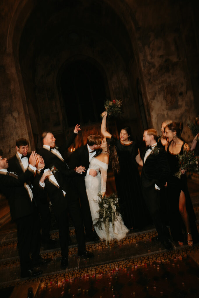A Family Photo at a Wedding of a  bride and groom kiss as their wedding party cheers around them at their wedding at The Mount Without in Bristol. 