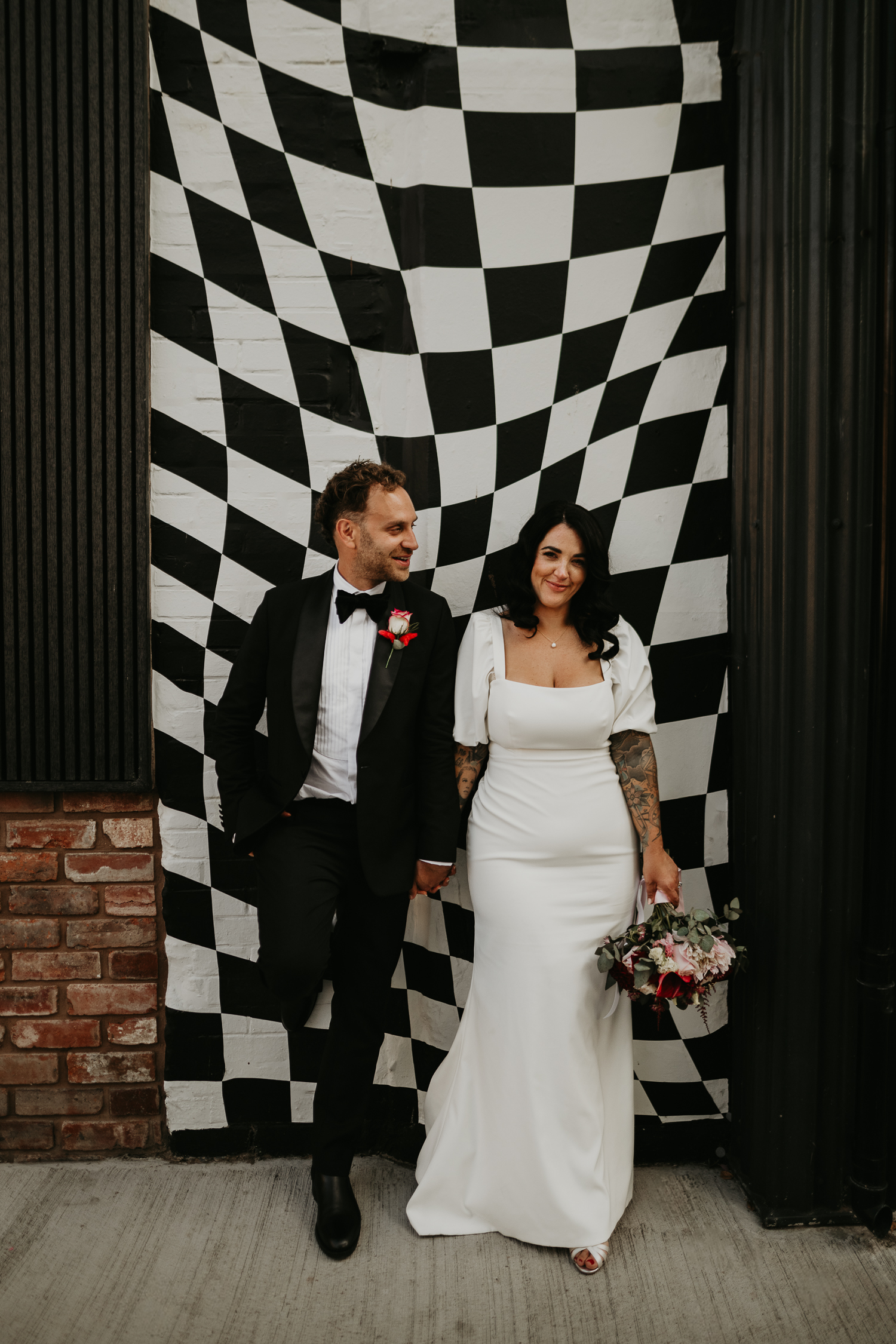 Wedding couple pose in front of the black and white checked mural at the shack revolution.